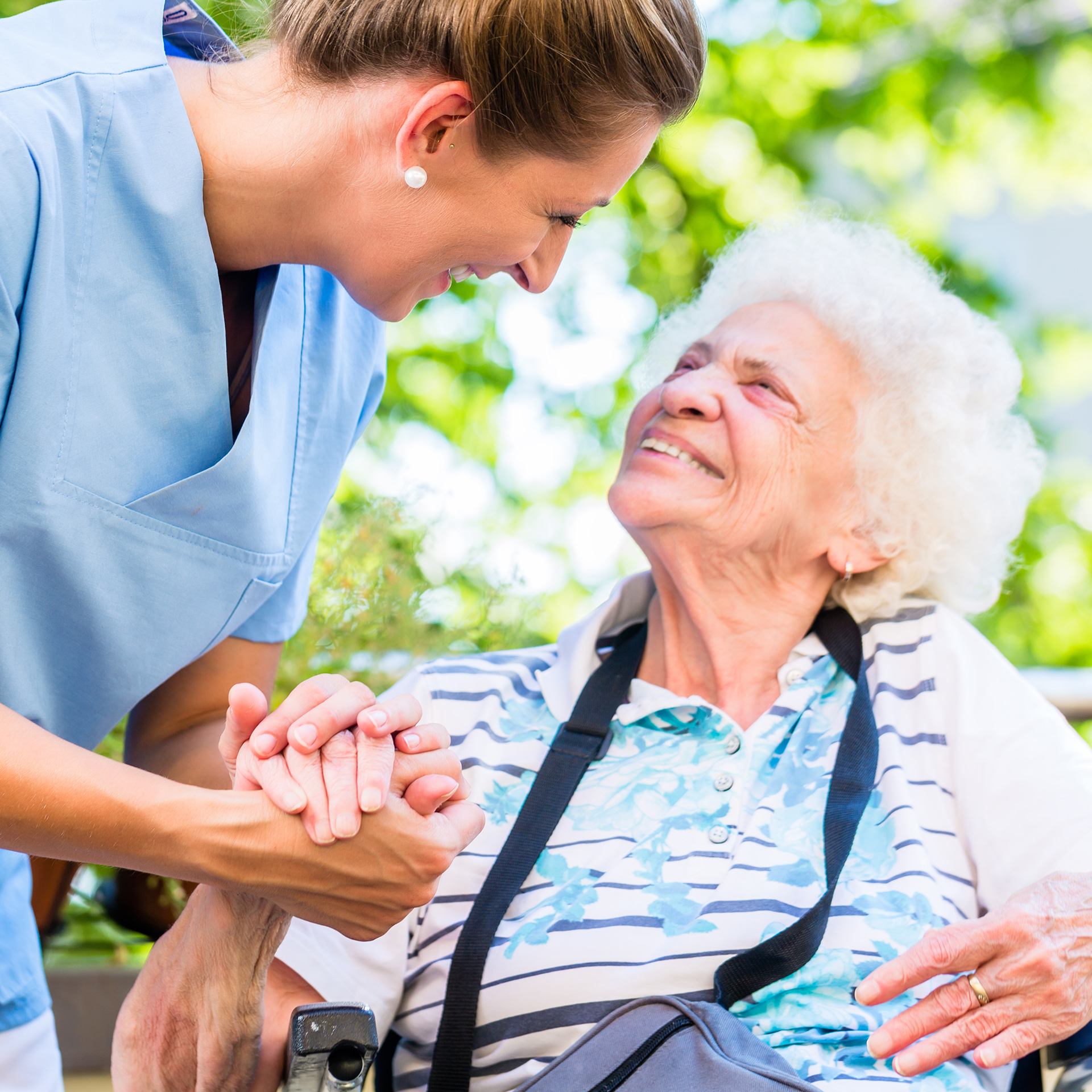 Pflegekraft hält Hand von älterer Dame im Rollstuhl